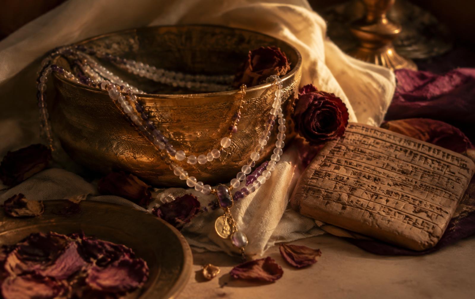 Gemstone necklaces in a brass bowl beside a clay tablet